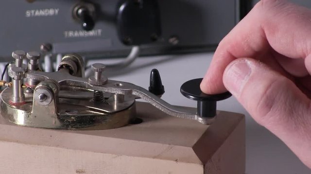 Extreme close-up of finger pressing telegraph key sending morse code radio transmission with vintage electronic hardware engineering military lab test equipment device in the background