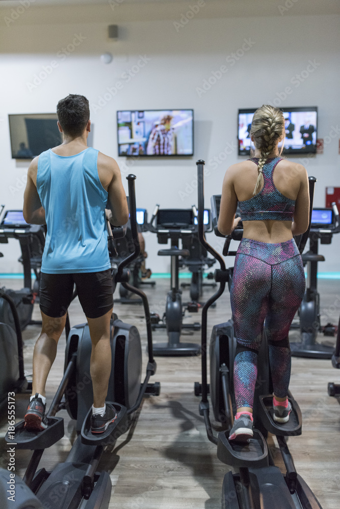 Wall mural TV training Couple training in elliptical bike while watching tv