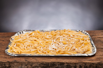 Raw handmade italian pasta tagliatelle on a wooden table. Black background