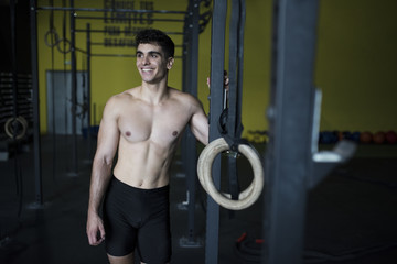 Fototapeta na wymiar The athlete: Fitness man posing near to ring in crossfit room