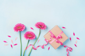 Spring composition with pink flowers and gift box on blue table top view. Greeting card for Birthday, Woman or Mothers Day. Flat lay.