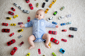 Adorable baby boy, lying on the floor, toy cars around him