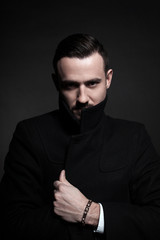 Portrait of a stylish young man in a black coat. Black background.