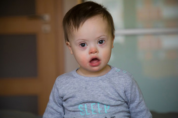 Portrait of cute baby boy with Down syndrome on the bed in home bedroom