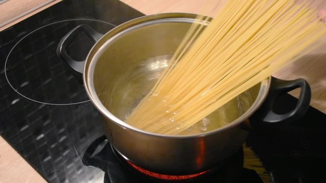Boiling water in a metal pan and lowering the long pasta spaghetti pasta into the water, cooking