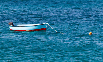A single small blue and red wooden traditional fishing boat moored up in the blue sea in Santa Maria, Sal, Cabo Verde Islands.