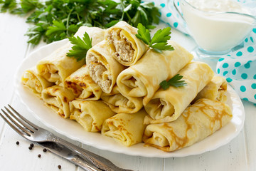 Pancake breakfast. Pancakes with meat stuffing, served with sour cream sauce on the kitchen wooden table.