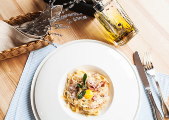 A beautiful serving of Italian Carbonara pasta with quail yolk and a bottle of olive oil on a wooden table