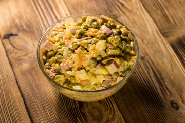 Mayonnaise salad with sausage, green pea, carrot and onion on wooden table