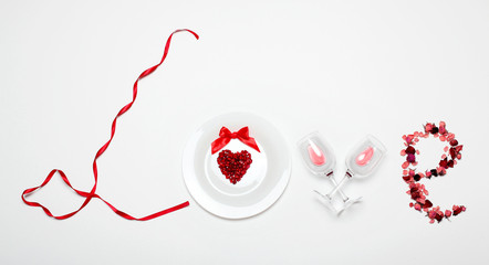 Love word of the red ribbon , white plate with Pomegranate seed in shape heart, glasses of wine, petals of dried roses on white background .Valentine's day creative background.Creative inscription