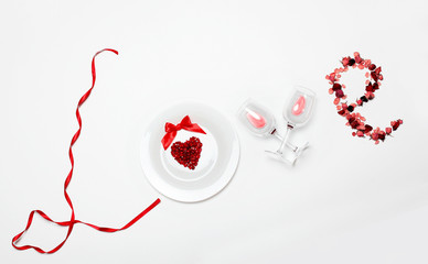 Love word of the red ribbon , white plate with Pomegranate seed in shape heart, glasses of wine, petals of dried roses on white background .Valentine's day creative background.Creative inscription