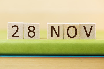 Wooden cube shape calendar for NOV 28 on green book, table.