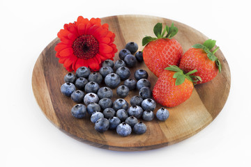 Blueberries and strawberries and a red flower on a wooden plate