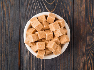 cubes of cane sugar in white bowl on wooden table, close-up, side view