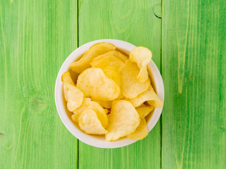 potato chips in white bowl on wooden table bright green