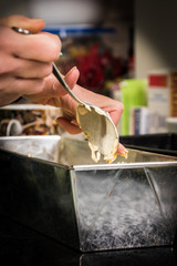 A woman's hand pouring cake batter ad dough into a baking form with a silver spoon. - 186578329