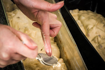 A woman's hand and fingers scraping cake batter and dough from a silver spoon into a baking form in a modern home kitchen. - 186578368