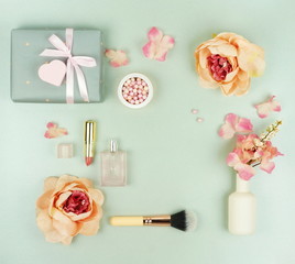 Obraz na płótnie Canvas Valentine's day concept background. Makeup cosmetic accessories products pearl make up powder and brush, lipstick, perfume, flowers, gift on pale grey background. Flat lay. Top view. Copy space