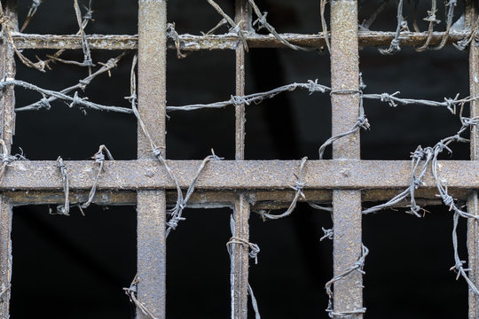 Rusty iron bars and barbed wire on a dark, depressive background