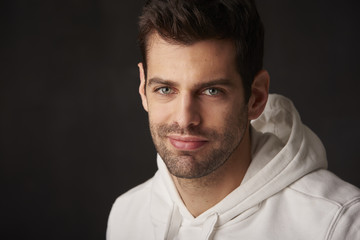 Studio shot of a handsome young man sitting at dark background while looking at camera and smiling.