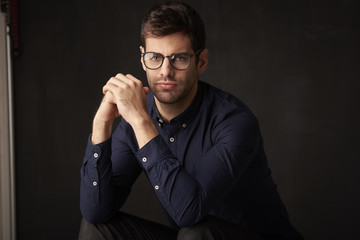 Young man studio portrait. Close-up shot of a young businessman standing at dark background and looking at camera. 