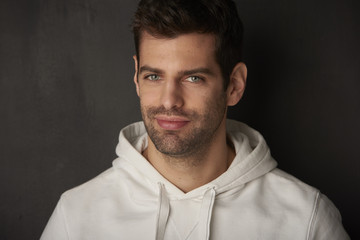 Studio shot of a handsome young man sitting at dark background while looking at camera and smiling.
