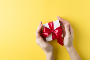 Womman's hand holding a gift box over yellow background, valentines theme