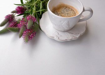Beautiful simple background of a white porcelain cup with coffee with a bouquet of pink spring wild flowers on a white background.