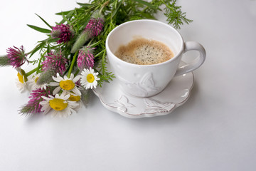 Background of beautiful white porcelain cup with coffee and a bouquet of forest flowers . suitable for a postcard or invitation for spring events with a place to be inscribed.