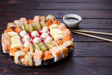 Tasty appetizing multicolored sushi rolls set, served with soy sauce and chopsticks on wooden table, copy space