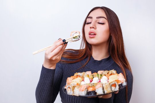 Young beautiful woman enjoy eating sushi, studio shoot on white background with copy space. Japanese food