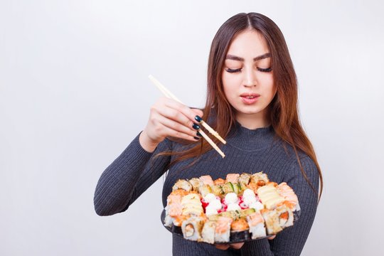 Young beautiful woman with chopsticks and sushi set, studio shoot on white background with copy space. Japanese food