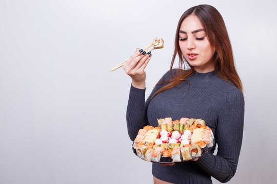 Young beautiful woman eating sushi, studio shoot on white background with copy space. Japanese food