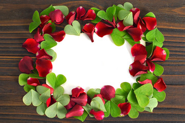 Valentines Day background with frame of red rose petals and heart shaped leaves
