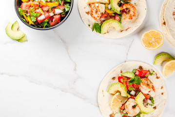 Seafood. Mexican food. Tortilla tacos with traditional homemade salsa salad, parsley, fresh lemon, avocado and grilled shrimp pawns. On a white marble background. Top view copy space