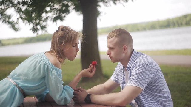 Happy Lover on a date by the river. Girl feeds boyfriend strawberries