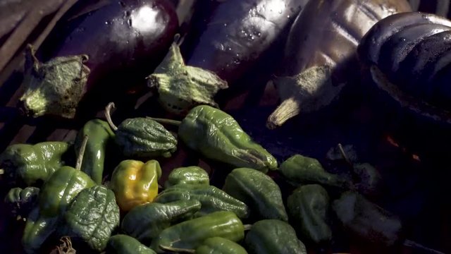 Picking up and turning eggplants and padron peppers on the grill roasting.