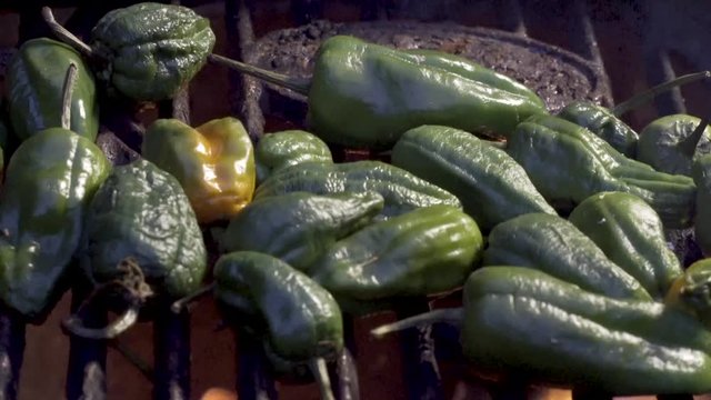 Flames licking padron peppers on the grill while the camera slides to the right.