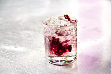Elegant cranberry cocktail with edible blossom, showcased on a textured metallic surface — refined and perfect for sophisticated lounges.