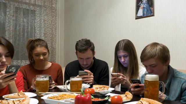 Group of friends at dinner party with all people on the table occupied with cellphones. friends with smartphones dining at home. technology and internet addiction concept