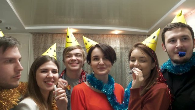 Friends with party hat blowing and having fun. Friends with party hats and festive noisemakers at party looking at camera and having fun. Young people having fun at birthday party