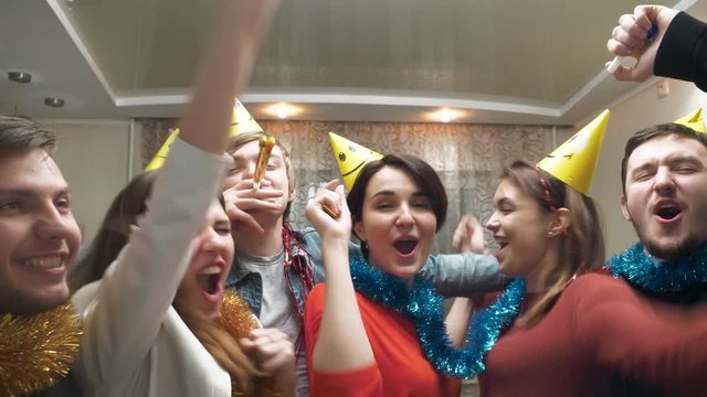 Friends with party hat blowing and having fun. Friends with party hats and festive noisemakers at party looking at camera and having fun. Young people having fun at birthday party