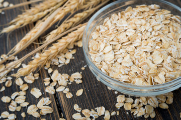 Raw oat flakes or oatmeal cereals in glass plate with oat spikes or spikelets