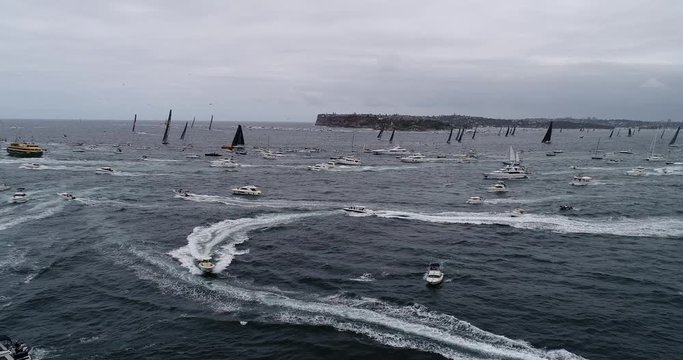 Yacht Race Sydney Hobart clearing Sydney Harbour south head in aerial moving backwards over crowd of boats and yachts.
