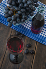 A wineglass of young red wine with glass bottle and a bunch of grapes