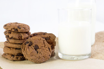 Chocolate chip cookies on brown paper and sack cloth with glass of milk on white background. With copy space for text.