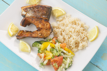 Pieces of fried fish, lemon, rice, vegetable salad, top view, on a blue background
