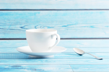 white mug with saucer and tea spoon on a blue background