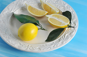 fresh yellow lemons with leaves on a plate on blue wooden background