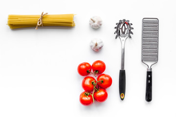 Cooking italian pasta. Spaghetti, tomatoes, garlic and cookware on white background top view copyspace